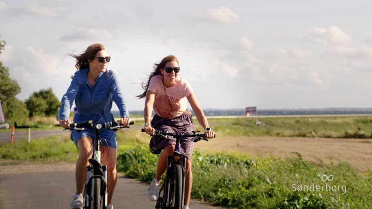 Two women cycling in good weather in the nature of Sønderborg municipality